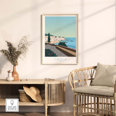 Framed Costa Brava Calella Spain poster displayed in a stylish interior with rattan furniture.